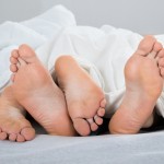 Feet Of Couple With Blanket In Bed